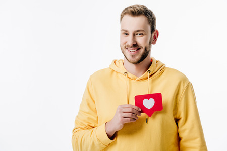 handsome cheerful man in yellow hoodie holding red paper cut card with heart symbol isolated on whiteの写真素材
