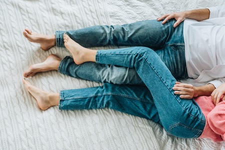Cropped view of man and woman in jeans lying on bedの写真素材