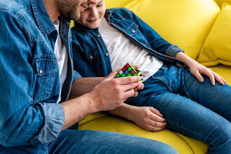 Partial view of father and son playing with toy cube while sitting on couch