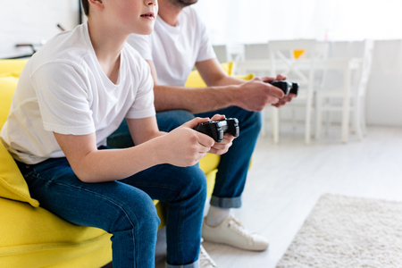 Cropped view of father and son playing Video Game on couch in Living Room