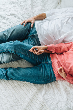 Cropped view of man and woman holding hands while lying on bedの写真素材