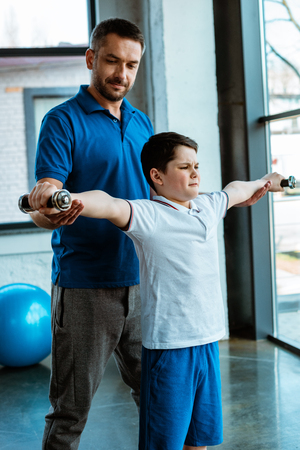 Father helping son working out with dumbbells at gymの写真素材