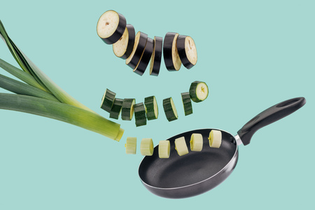 Fresh sliced organic vegetables above pan isolated on turquoise backgroundの写真素材