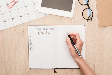Partial view of recruiter holding pen near notebook with exit interview checklist letteringの写真素材