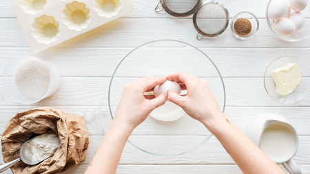 Partial view of woman cracking egg in bowl while cooking on tableの写真素材