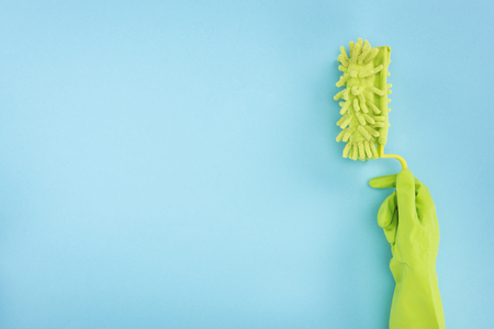 Cropped view of cleaner in green rubber glove holding sponge on blue background