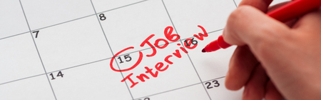 Panoramic shot of man writing with red marker on calendar with job interview letteringの写真素材