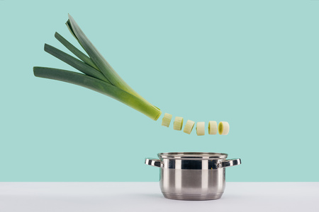 Green fresh sliced leek above saucepan on white surface isolated on turquoise backgroundの写真素材