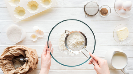 Cropped view of woman sieving flour in bowl on table with ingredientsの写真素材