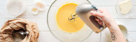 Panoramic shot of woman mixing dough with hand mixer on wooden table