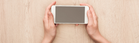 Panoramic shot of woman holding smartphone with blank screen at wooden tableの写真素材