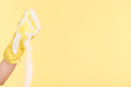Cropped view of cleaner in yellow rubber glove squeezing sponge with foam on yellow backgroundの写真素材