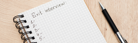 Panoramic shot of notebook with exit interview lettering and numbers on wooden surface with penの写真素材