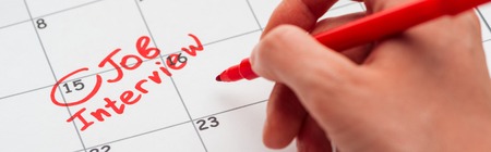 Panoramic shot of man writing with red marker on print calendar with job interview letteringの写真素材