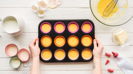 Cropped view of woman holding muffin mold with liquid dough on table with ingredients
