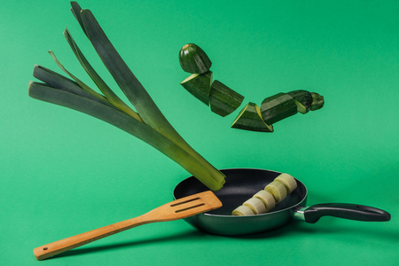 Fresh organic sliced green leek and zucchini in frying pan on green backgroundの写真素材