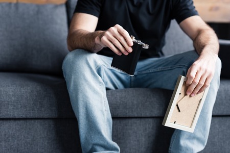 Partial view of man sitting on grey sofa and holding photo frame and flask with alcoholの写真素材