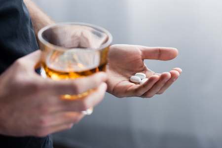 Partial view of standing man holding handful of pills and glass of whiskeyの写真素材