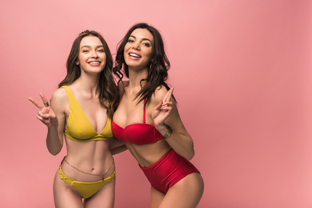 Two pretty girls in bikini showing peace signs isolated on pink backgroundの写真素材