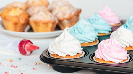 Delicious cupcakes with colorful frosting and sprinkles in cupcake trayの写真素材