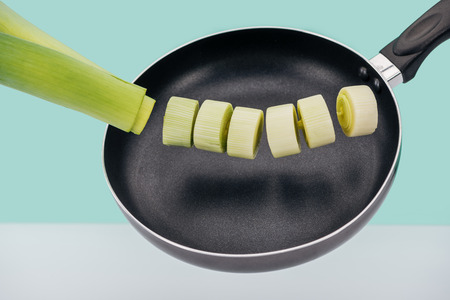 Fresh green leek in frying pan isolated on turquoise background