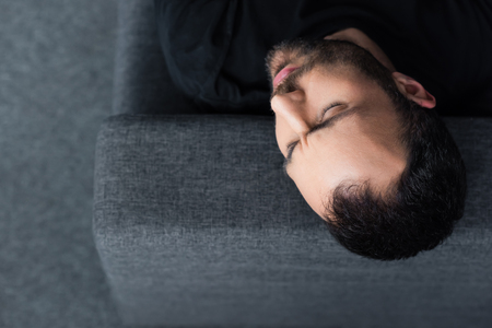 Overhead view of lonely man lying on grey sofa with closed eyesの写真素材