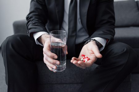 Cropped view of man in black suit holding glass of water and handful of pillsの写真素材