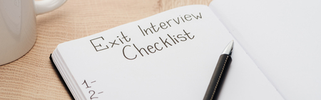 Panoramic shot of notebook with exit interview checklist lettering and numbers on wooden table with...