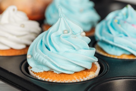 Close up of delicious blue cupcakes decorated with sprinkles in cupcake trayの写真素材