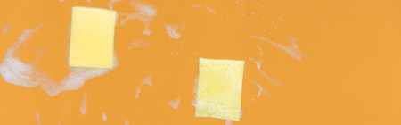 Panoramic shot of of yellow sponges with foam on orange background