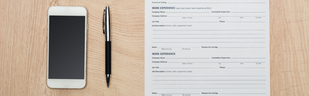 Panoramic shot of pen, smartphone with blank screen and resume template on wooden surface