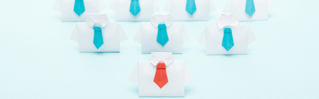 Panoramic shot of origami white shirts with blue ties with one red on blue background, leadership conceptの写真素材