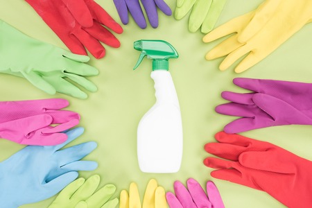 Top view of multicolored rubber gloves in circle around spray bottle with detergent on green backgroundの写真素材