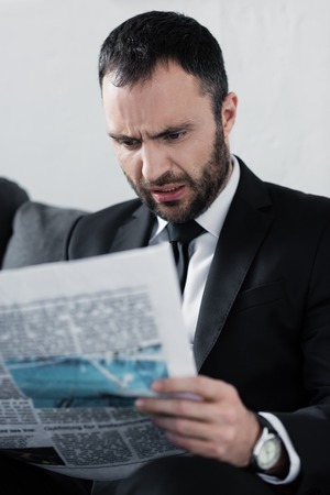 Selective focus of shocked bearded businessman reading newspaperの写真素材