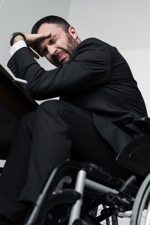 Low angle view of depressed businessman crying while sitting in wheelchairの写真素材