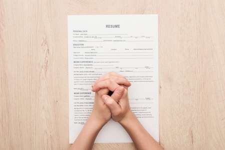Partial view of recruiter holding clenched hands on resume template on wooden tableの写真素材