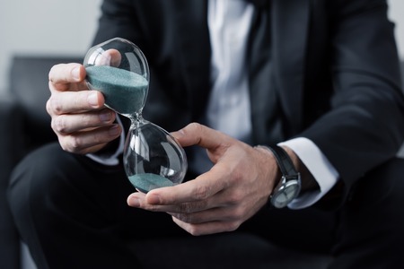 Cropped view of sitting man in suit holding hourglassの写真素材