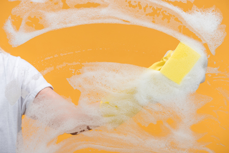 Cropped view of cleaner in rubber glove cleaning glass with sponge on orange backgroundの写真素材