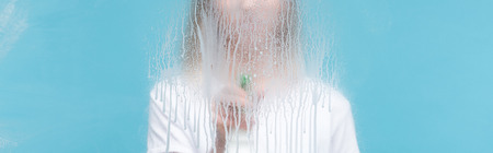 Panoramic shot of young woman cleaning glass with dripping detergent on blue backgroundの写真素材