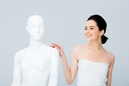 attractive smiling young woman in white posing with mannequin isolated on greyの写真素材