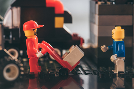 KYIV, UKRAINE - MARCH 15, 2019: lego postman figurine in hat moving package on hand truck near other lego figureのeditorial素材