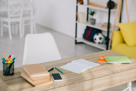 selective focus of wooden desk with books, stationery, copy books and smartphone with blank screenの写真素材