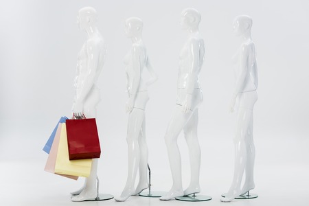row of white mannequins with shopping bags on greyの写真素材