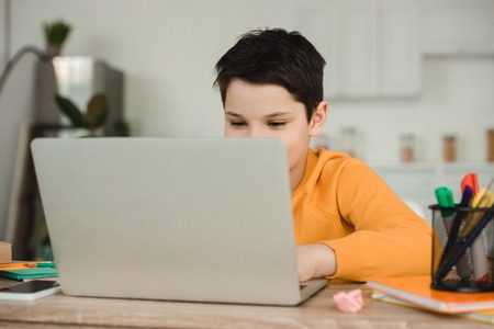 cute schoolkid using laptop while doing schoolwork at homeの写真素材