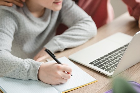 partial view of boy writing in notebook and using laptop near mother
