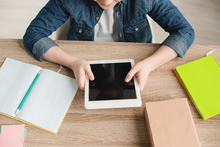 cropped view of boy holding digital tablet with blank screen while sitting at desk with notebooksの写真素材