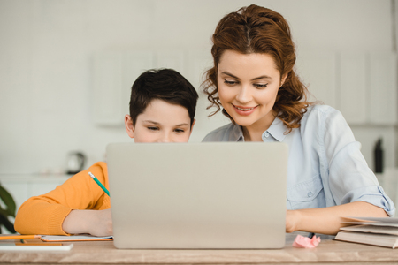 happy mother with cute son using laptop together while doing schoolwork at homeの写真素材
