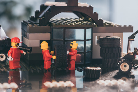KYIV, UKRAINE - MARCH 15, 2019: lego minifigures in red carrying tire while other figurine shouting in mouthpiece at service stationのeditorial素材