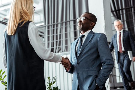 low angle view of blonde businesswoman shaking hands with african american businessmanの写真素材