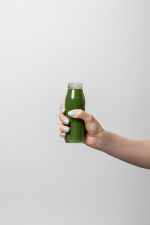 cropped view of woman holding glass bottle with tasty green smoothie on whiteの写真素材